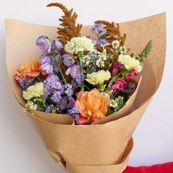 Bouquet of flowers wrapped in brown paper with a blue ribbon, held by a person wearing a red sleeve. available in sunshine coast