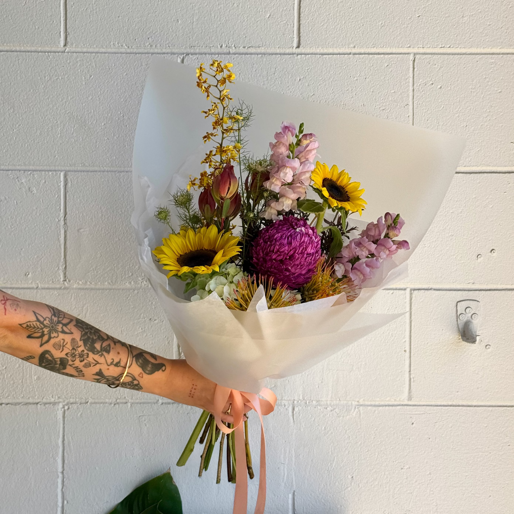 Person holding a bouquet of flowers against a white tiled wall