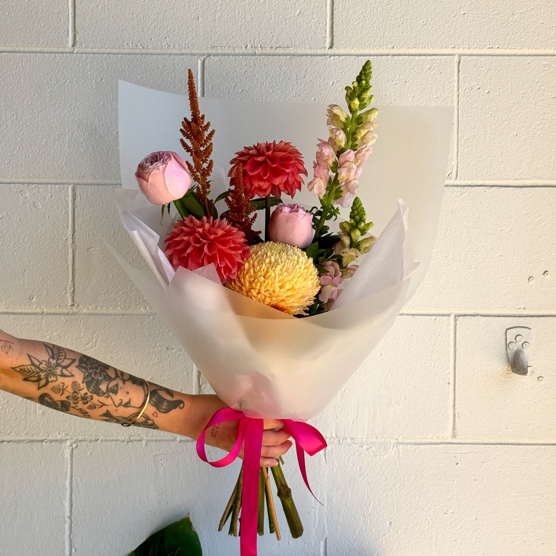 Bouquet of bright flowers held by a person against a tiled wall
