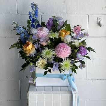 colourful flower arrangement in floral foam and a white box.
