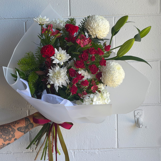 Bouquet of red and white christmas flowers with green leaves against a white tiled wall.