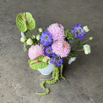Floral arrangement with pink, purple, and green flowers in a white vase on a concrete surface