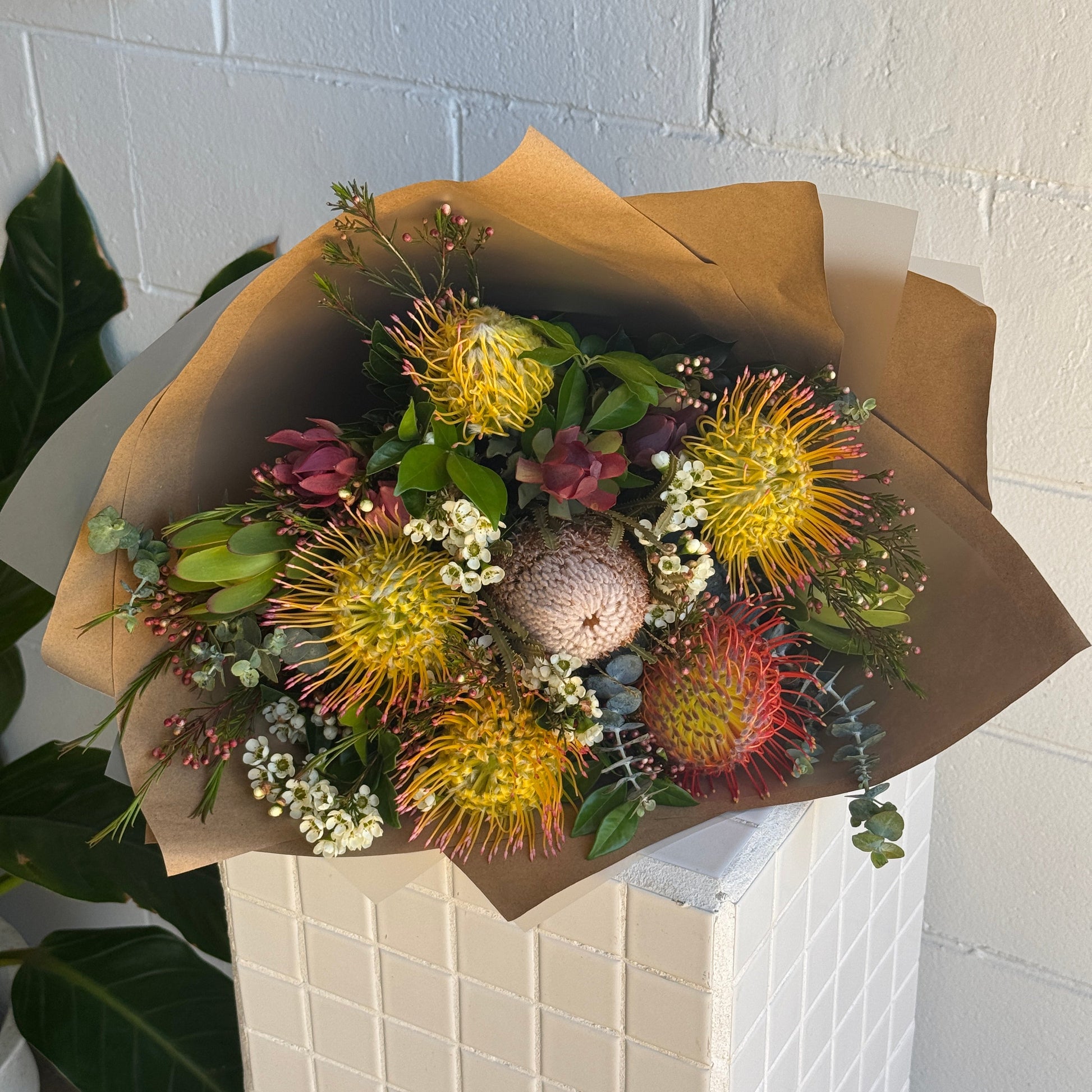 Bouquet of native flowers wrapped in brown paper on a white tiled floor.