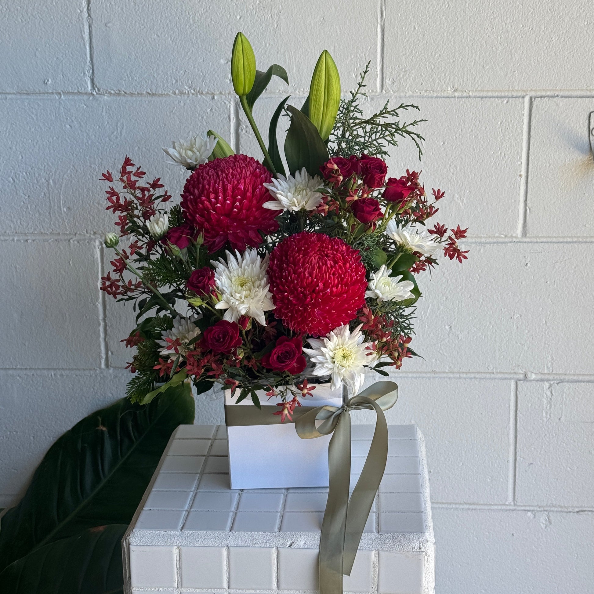 Christmas Floral arrangement with red and white flowers in front of a white tiled wall.