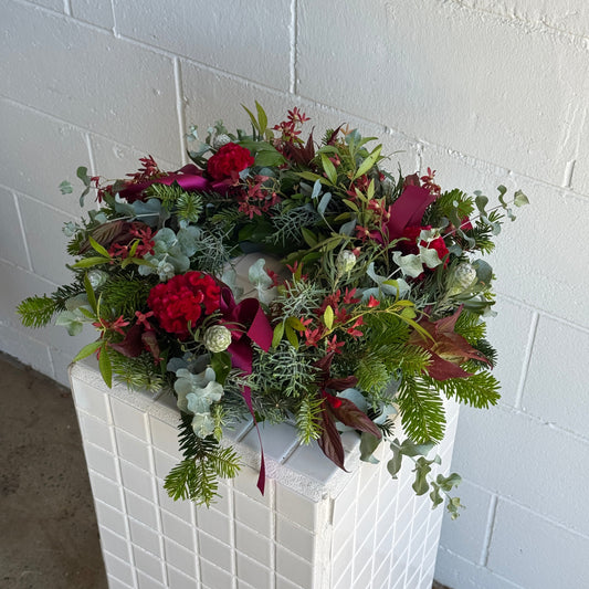 Decorative fresh christmas wreath with red flowers and greenery on a white surface.