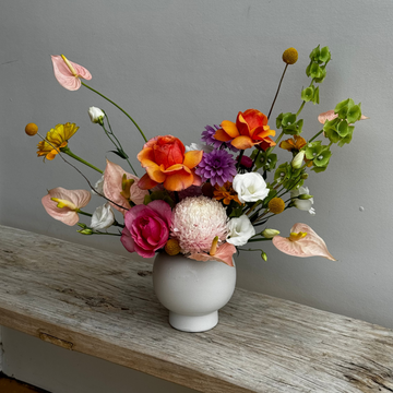 Floral arrangement in a white vase on a wooden surface with a gray wall background in Caloundra